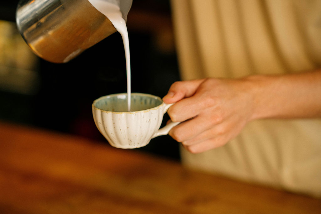 Handen die melk in een kopje koffie schenken op een houten bar