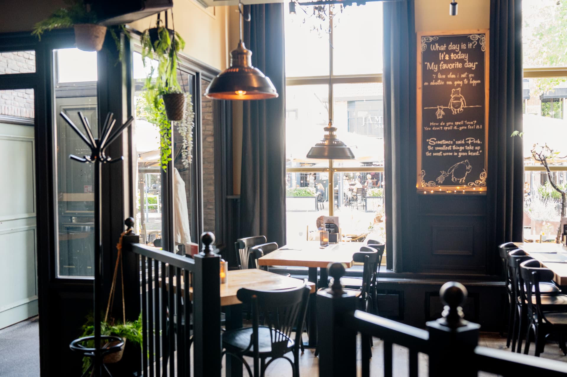 Grand café met houten tafels, bistrostoelen en een krijtbord aan de muur